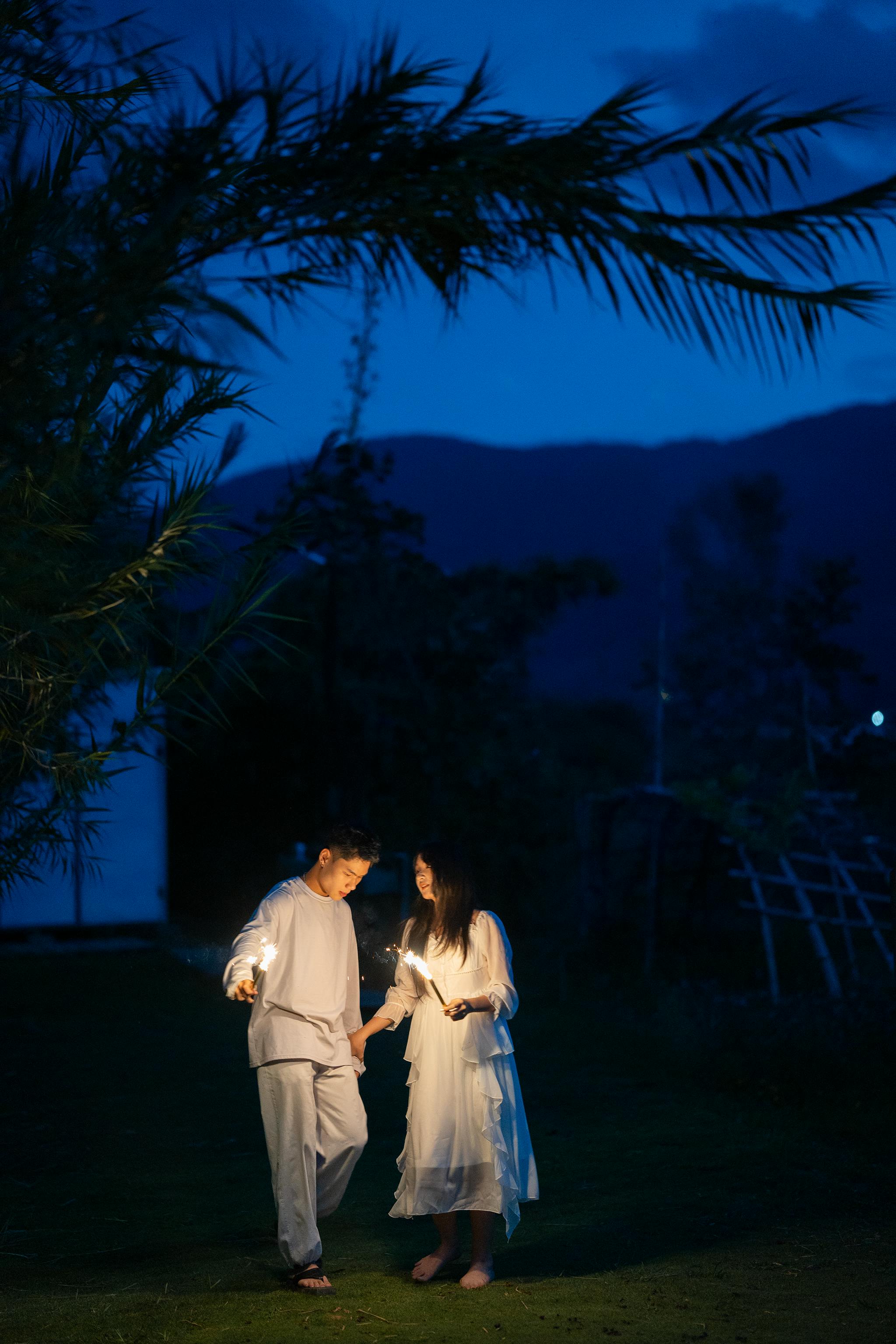 Couple enjoying a romantic evening walk with sparklers in Dalat, Vietnam, under a twilight sky.