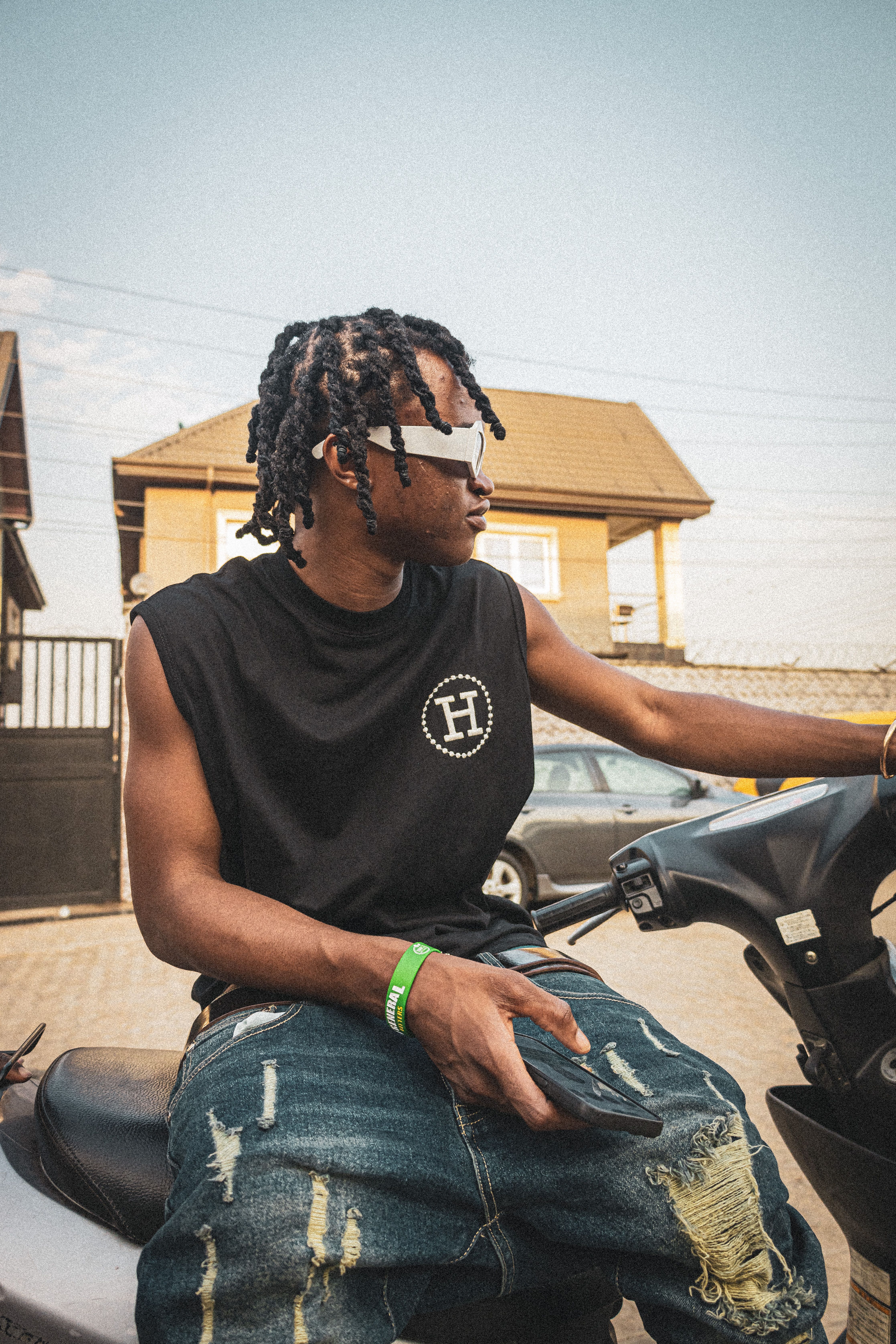 Stylish young man with dreadlocks and sunglasses sitting on a scooter outdoors.