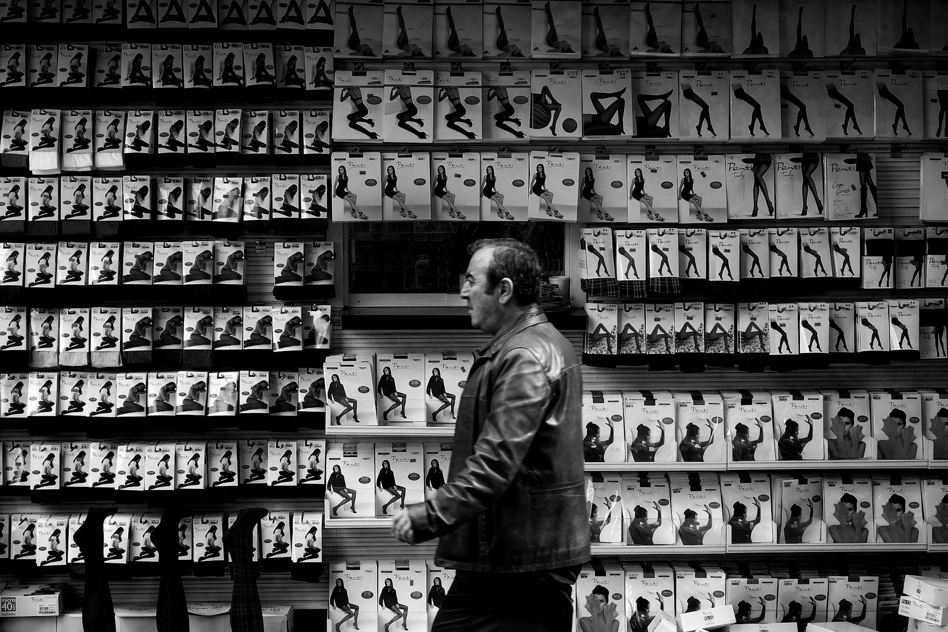 A man walks past a wall of packaged stockings in a monochrome store setting, creating a striking visual contrast.