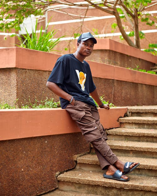 Young Man in Black T-Shirt and Brown Pants Posing on Stairs in Park