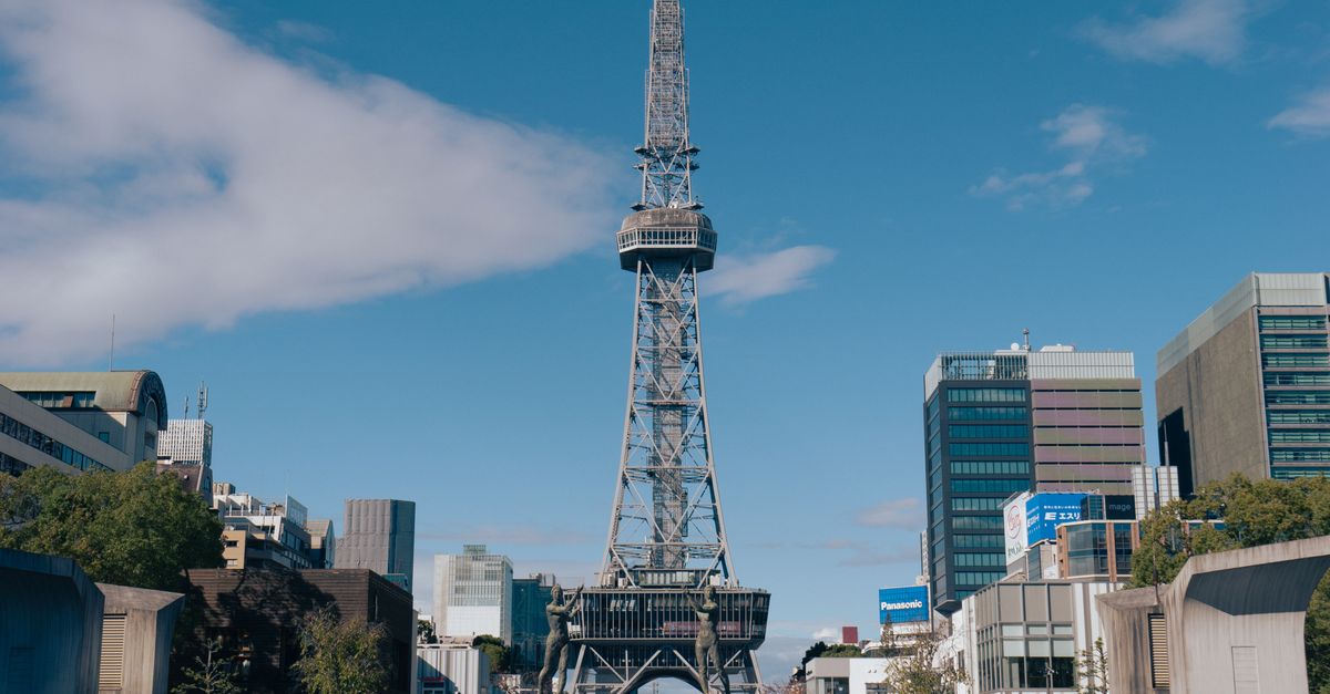A view of Nagoya TV Tower surrounded by urban buildings under a clear blue sky.