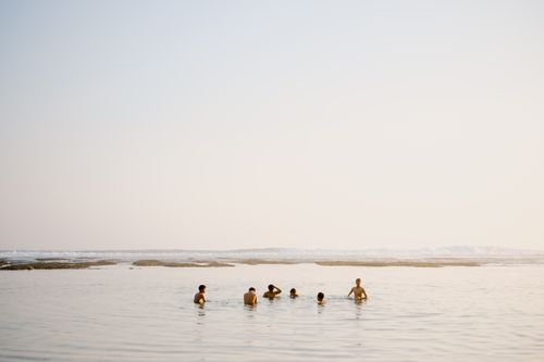 Free A group of young adults enjoying a swim in the calm sea at sunset, reflecting leisure and summertime vibes. Stock Photo