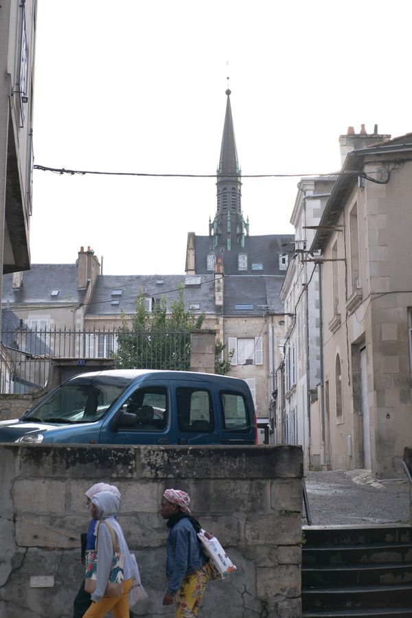Femmes passant devant un mur de pierre sous un clocher