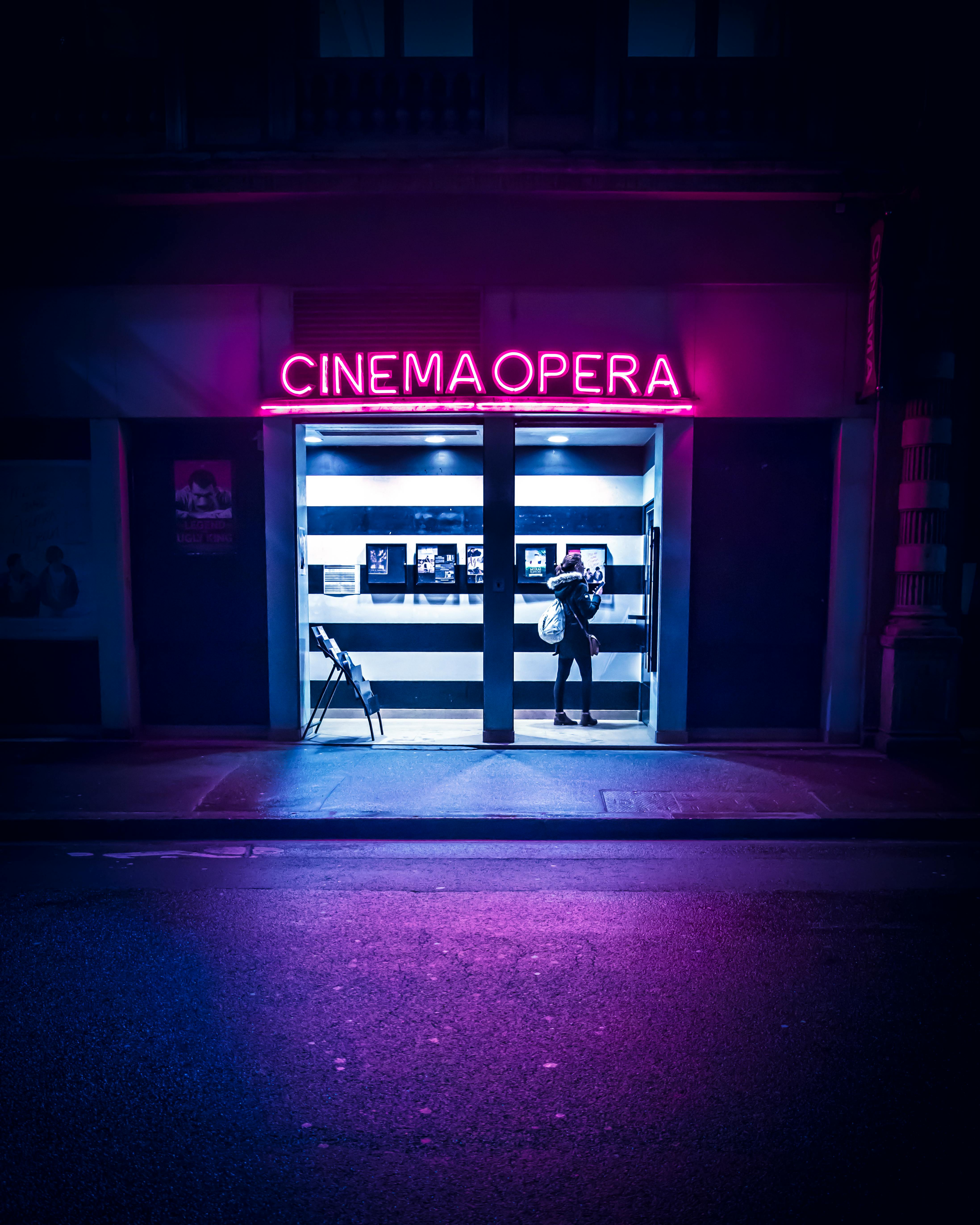 Free Moody night scene of a neon-lit cinema entrance in Lyon, France, with a person standing outside. Stock Photo