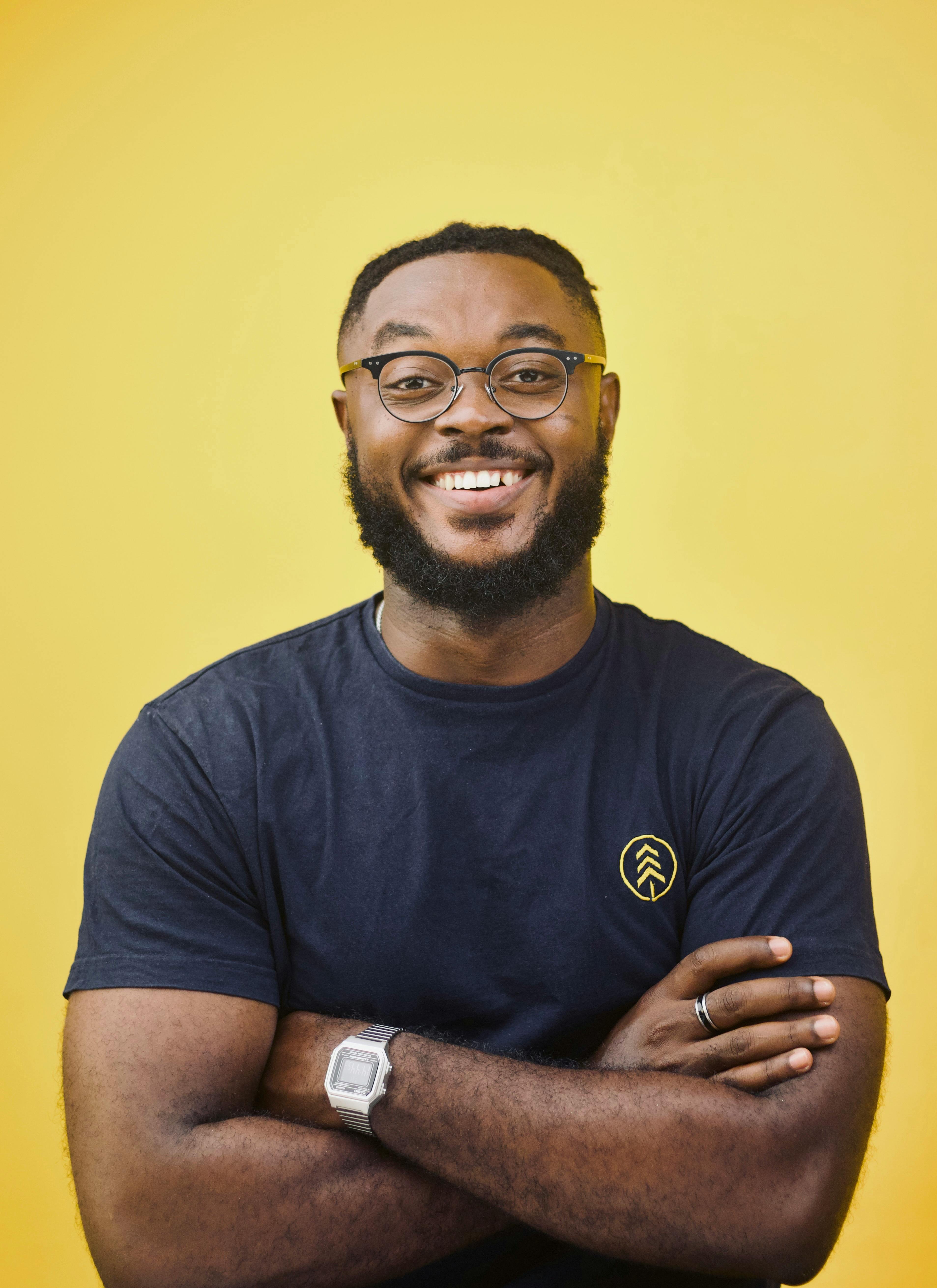 Cheerful man with glasses and a beard, wearing a t-shirt, smiling against a vibrant yellow backdrop.