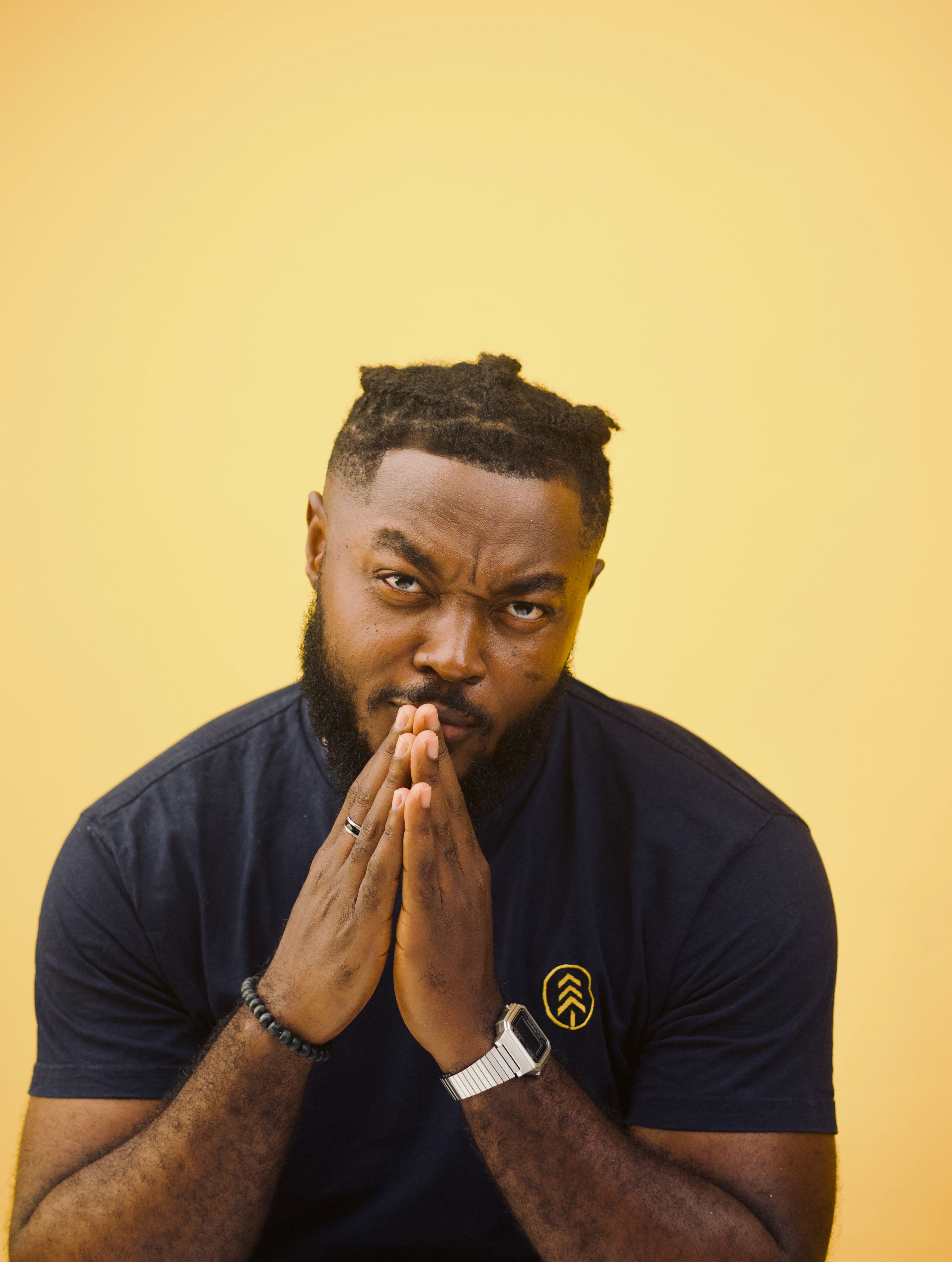 Fashionable male in a black t-shirt posing against a yellow background, conveying a thoughtful mood.