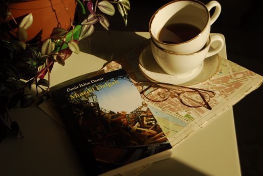Warm setting with book, coffee cup, glasses, and map for a cozy reading vibe.