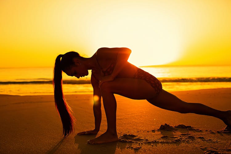 Woman Stretching On The Beach At Sunset 