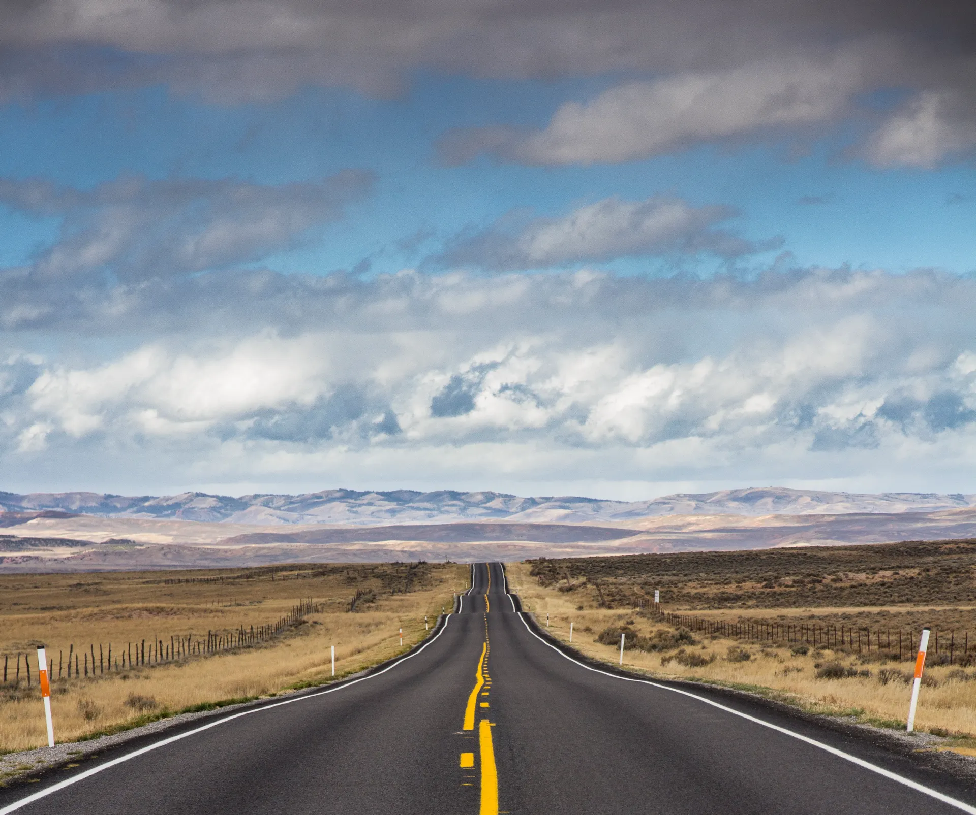 Dramatic view of a long, open road through a vast desert landscape under cloudy skies. Dramatic view of a long, open road through a vast desert landscape under cloudy skies.