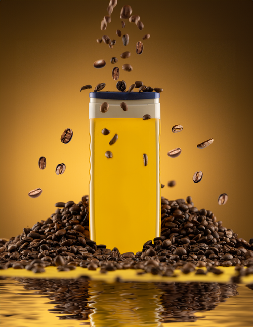 Free Bright yellow bottle surrounded by coffee beans in a dynamic studio shot with a reflective surface. Stock Photo