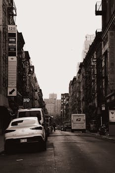 Moody New York City street with vehicles and pedestrians in black and white.