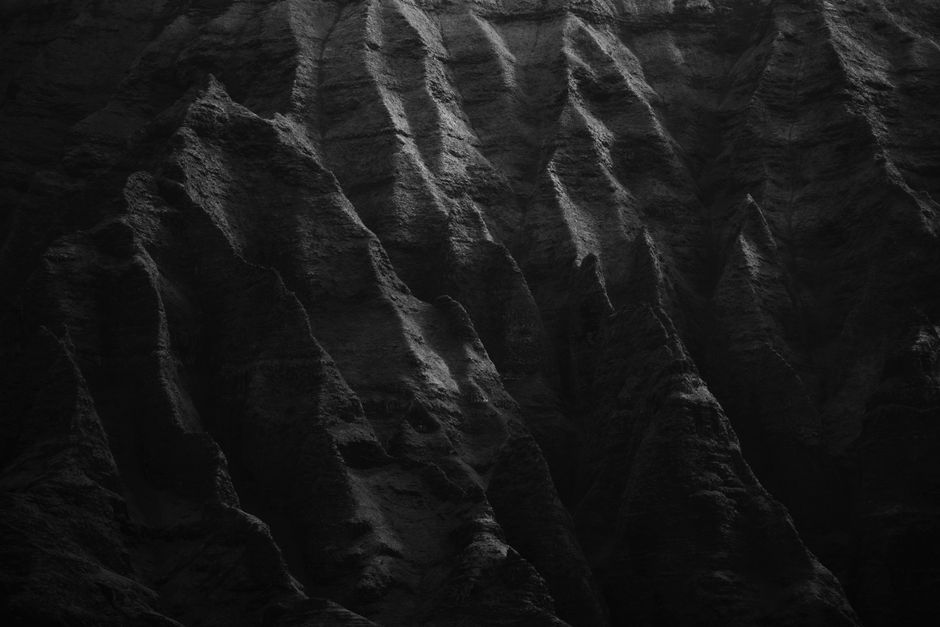 Dark and textured cliffs captured in black and white, showcasing natural patterns and rugged surfaces.