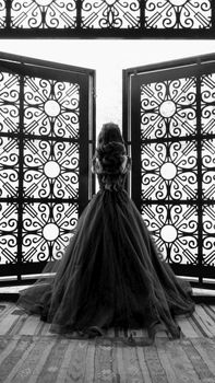 A woman in a black dress stands elegantly before decorative doors, embodying grace and sophistication.