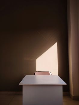 Minimalist office interior featuring a white desk with sunlight on the wall, creating a serene atmosphere.