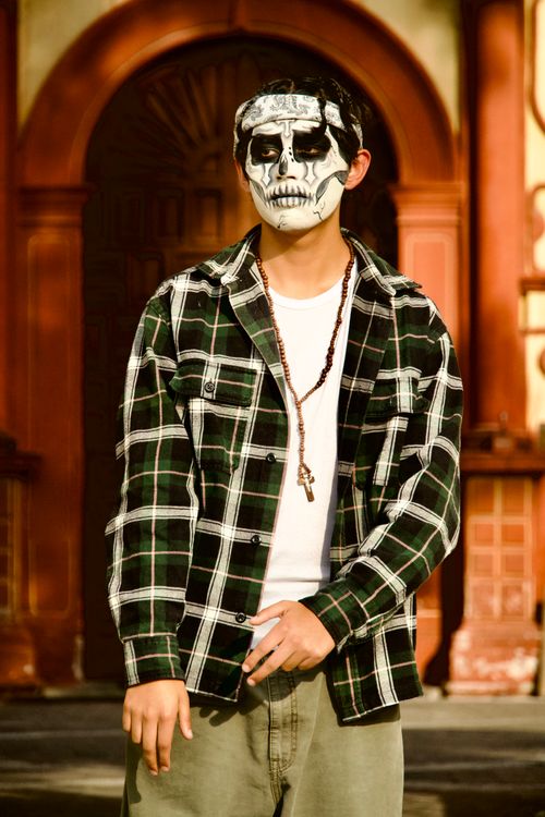 Free A person with skull face paint standing in front of a traditional Mexican building, embracing Day of the Dead traditions. Stock Photo