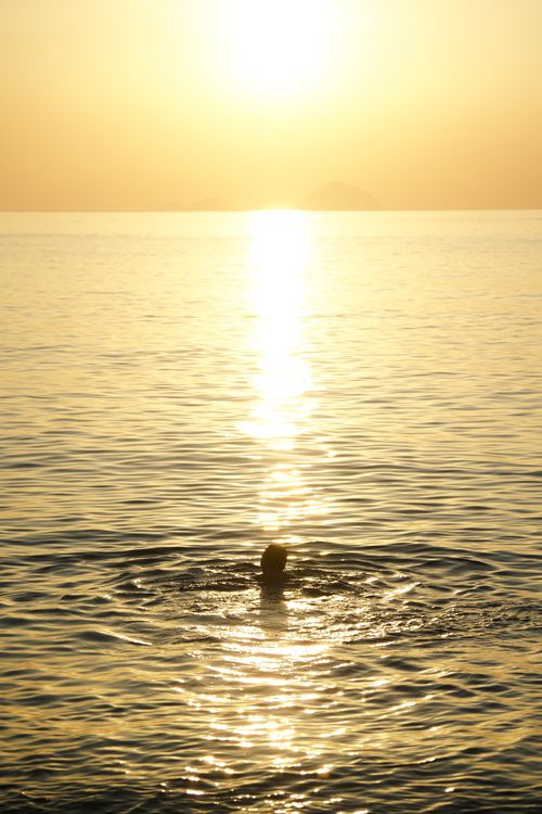 Free A lone swimmer enjoys the tranquil sea at sunset in Nha Trang, Vietnam. Stock Photo