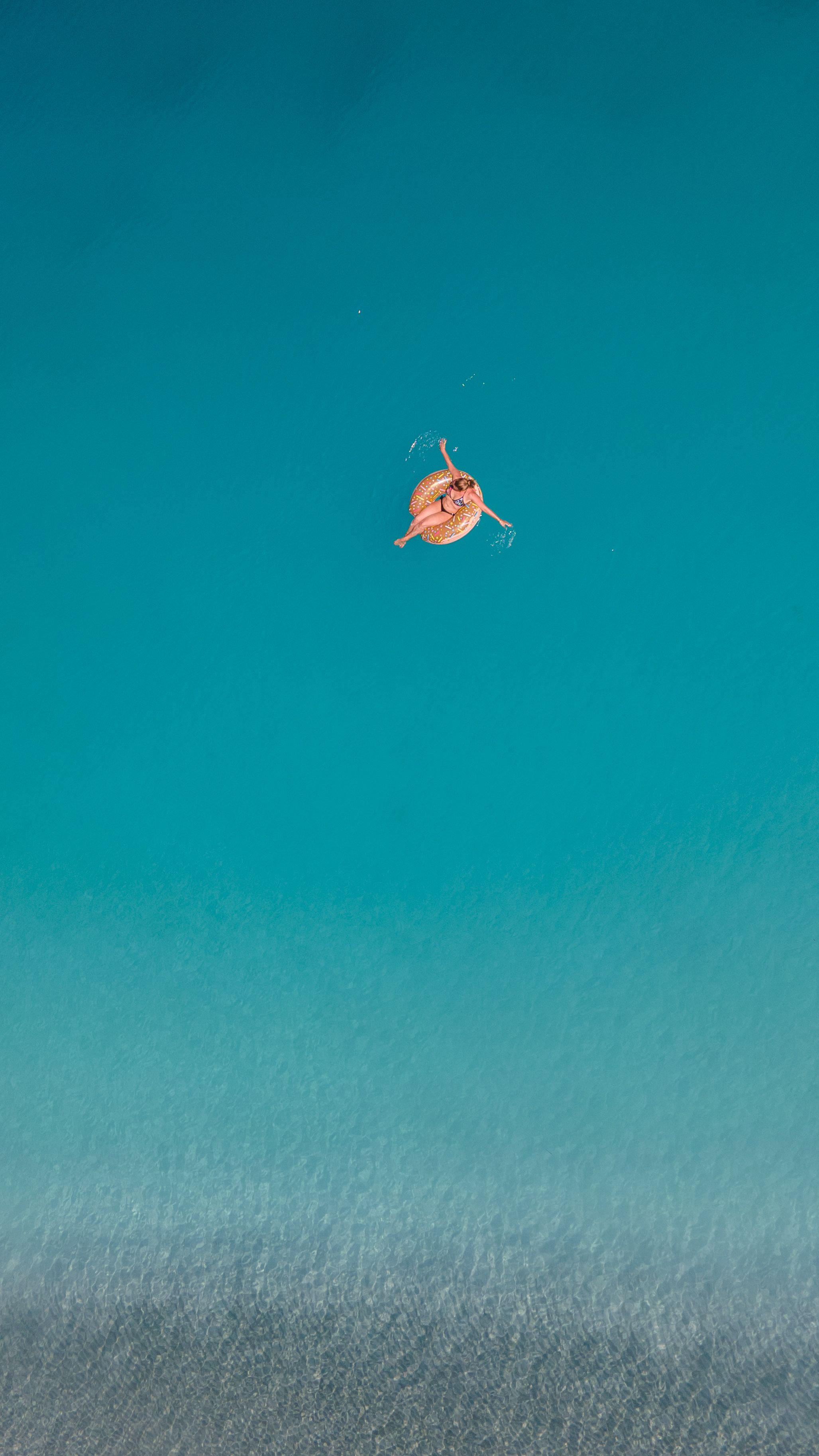 Top-down view of a woman lounging on a swim ring in clear blue waters, capturing relaxation and summer vibes.