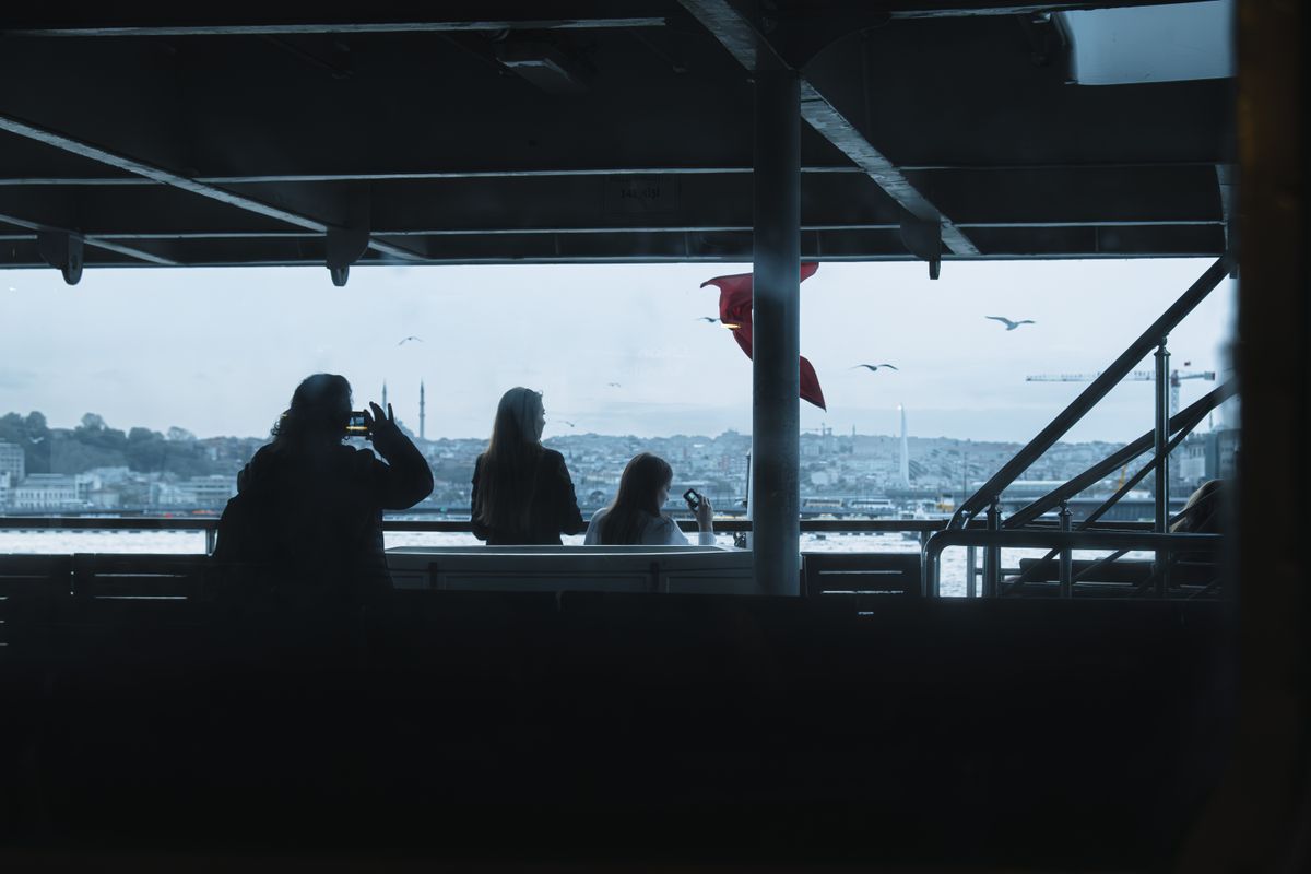 Passengers silhouetted on a ferry in Istanbul with cityscape background.