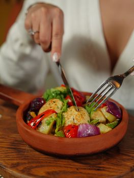 Close-up of a woman cutting into a vibrant vegetable dish in a cozy setting.