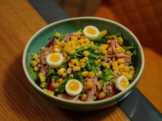 Green bowl of flaked tuna, sweet corn, halved quail eggs, arugula and cherry tomatoes