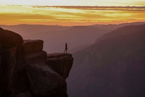 Free A single person stands on the edge of a cliff during a vibrant sunset, capturing the spirit of adventure and freedom. Stock Photo