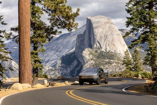 Electric vehicle driving on a winding road in Yosemite with Half Dome in the background.