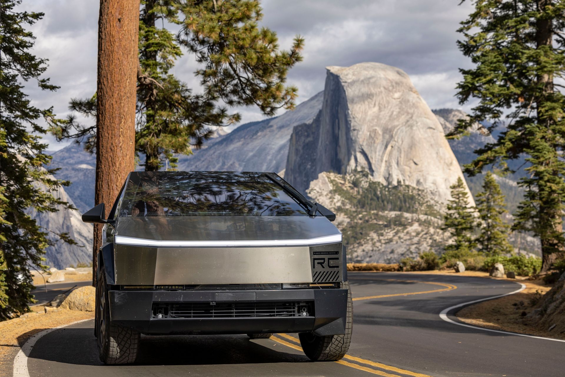 Futuristic vehicle on a winding road with mountain and trees, showcasing modern transportation in nature.