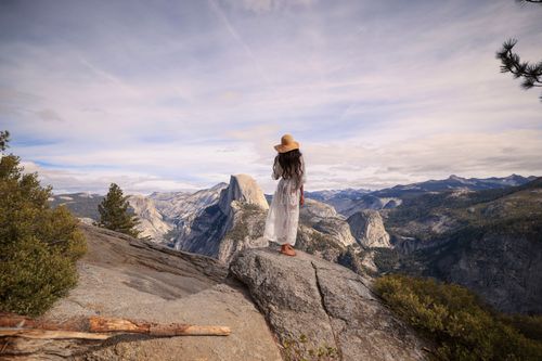 Free Elegant woman in white dress on rock enjoying the iconic Half Dome in Yosemite National Park. Stock Photo