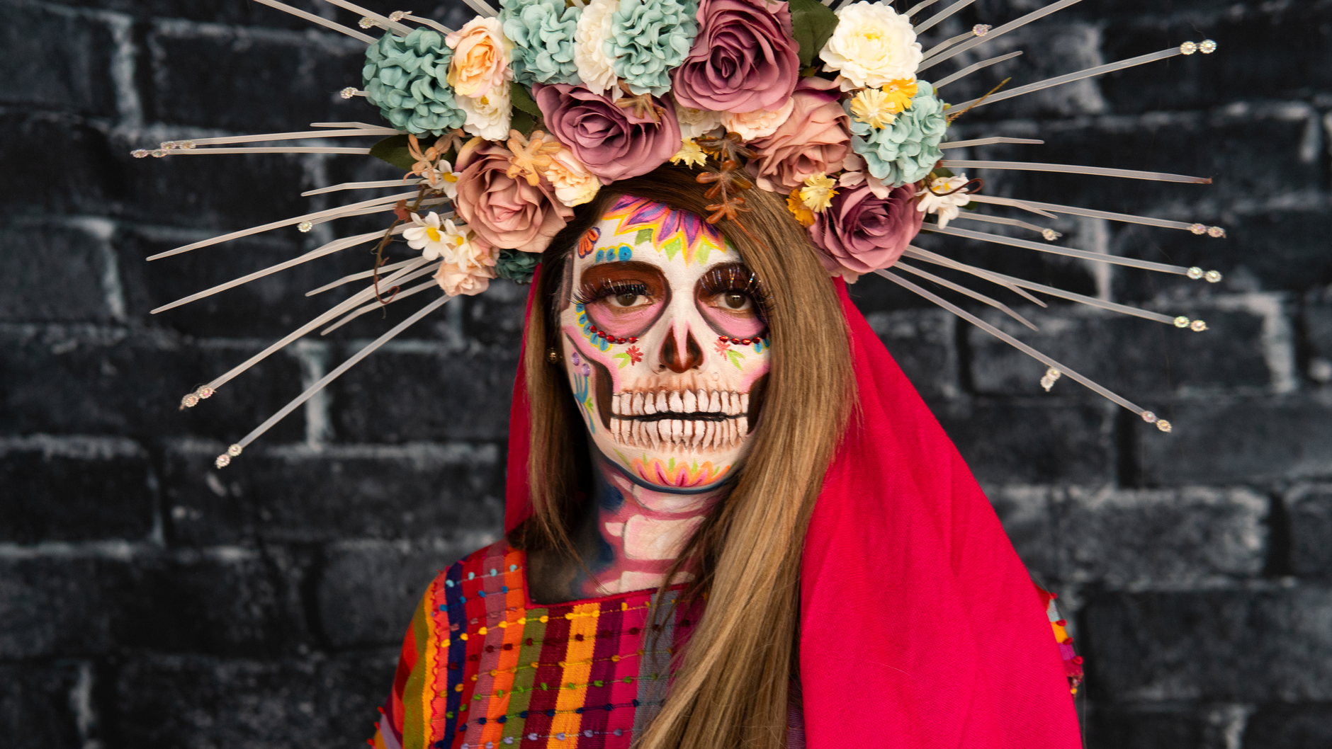 Colorful portrait of a woman in Dia de los Muertos costume with floral crown and skull makeup.