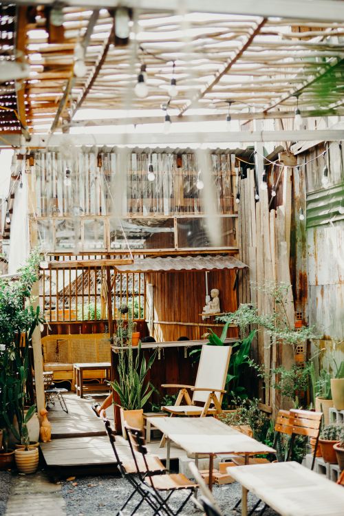 Free A charming outdoor patio with wooden tables and chairs surrounded by lush plants and natural light. Stock Photo