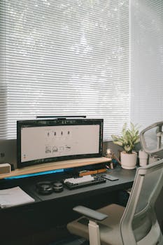 Contemporary office desk with computer, keyboard, and office chair by a window.