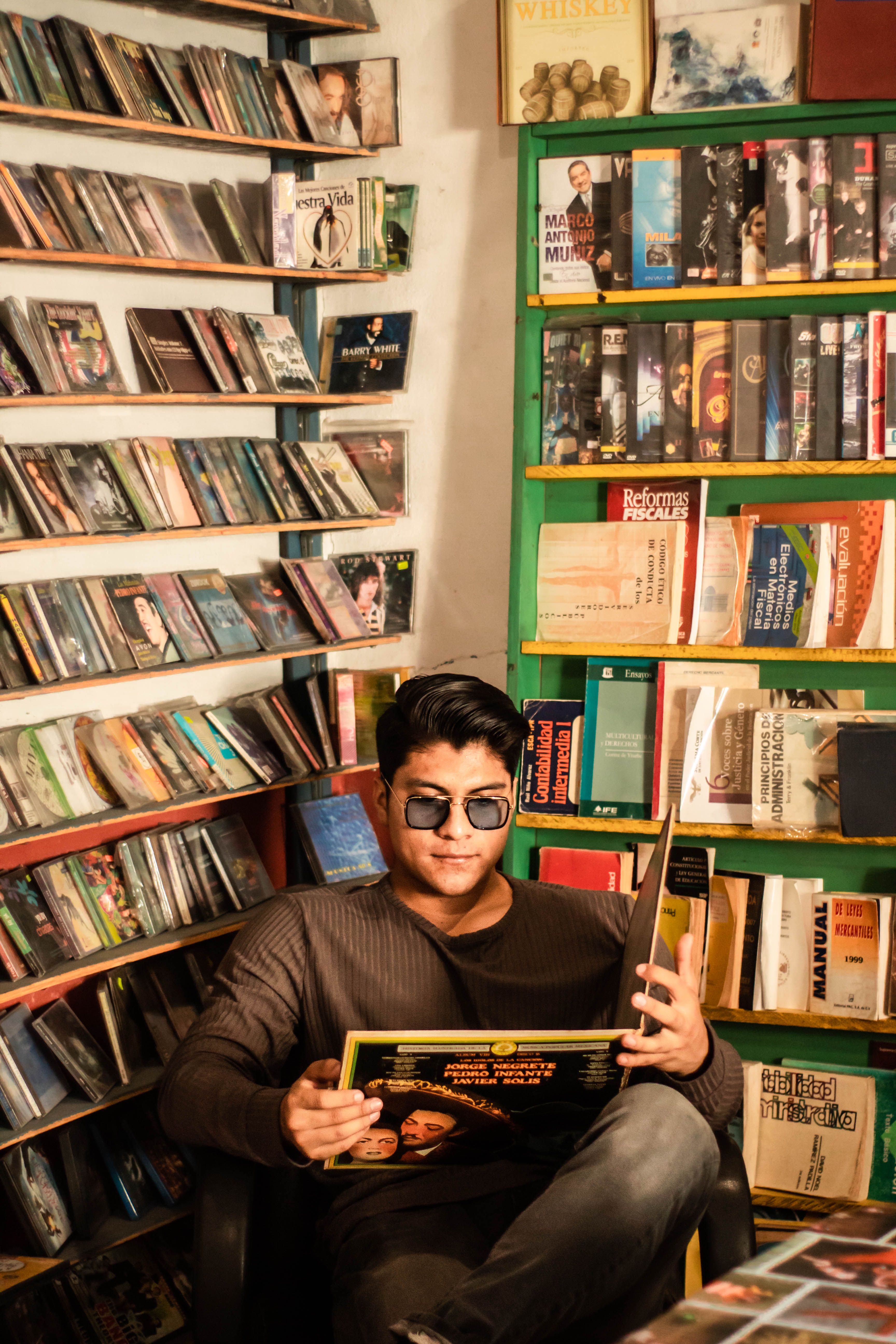 Young man reading in a cozy vintage bookstore corner, surrounded by diverse book selections.
