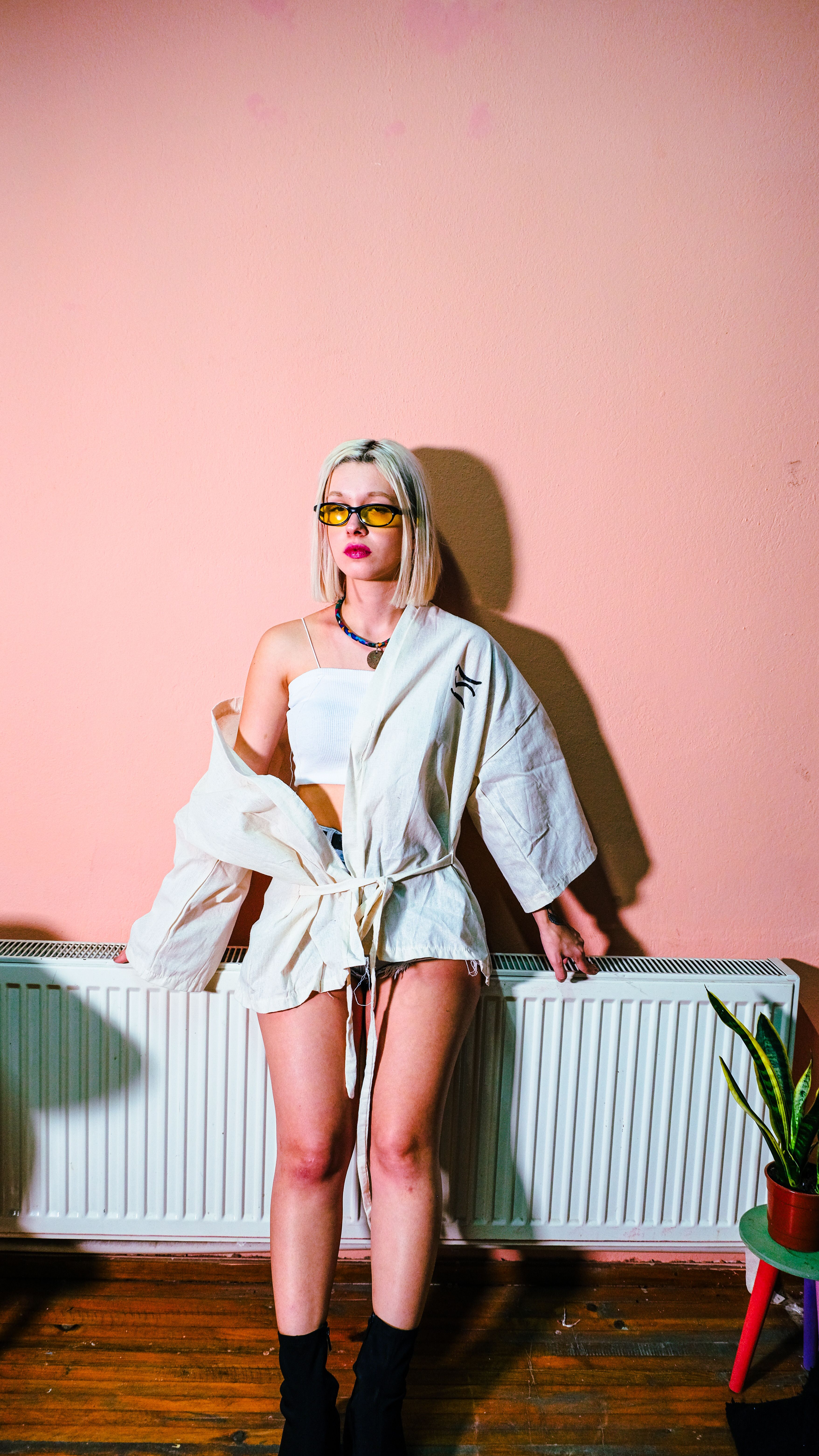Fashionable woman in a kimono poses indoors by a radiator, creating a modern aesthetic.