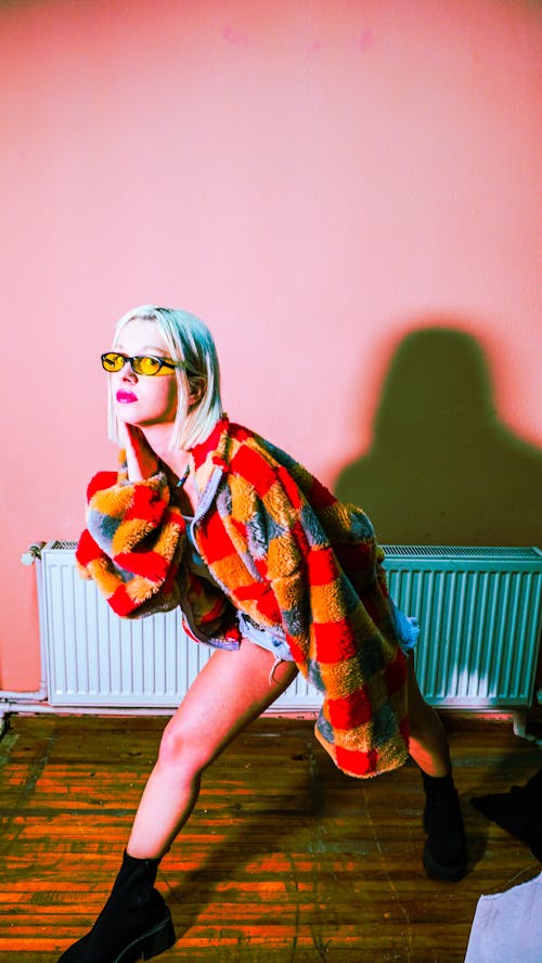 Blonde Woman Posing in Colorful Coat in Room with Pink Wall