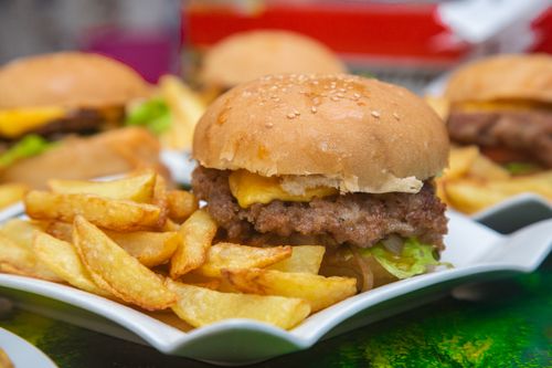 Free Appetizing cheeseburger with crispy fries served on a white plate, showcasing fast food indulgence. Stock Photo