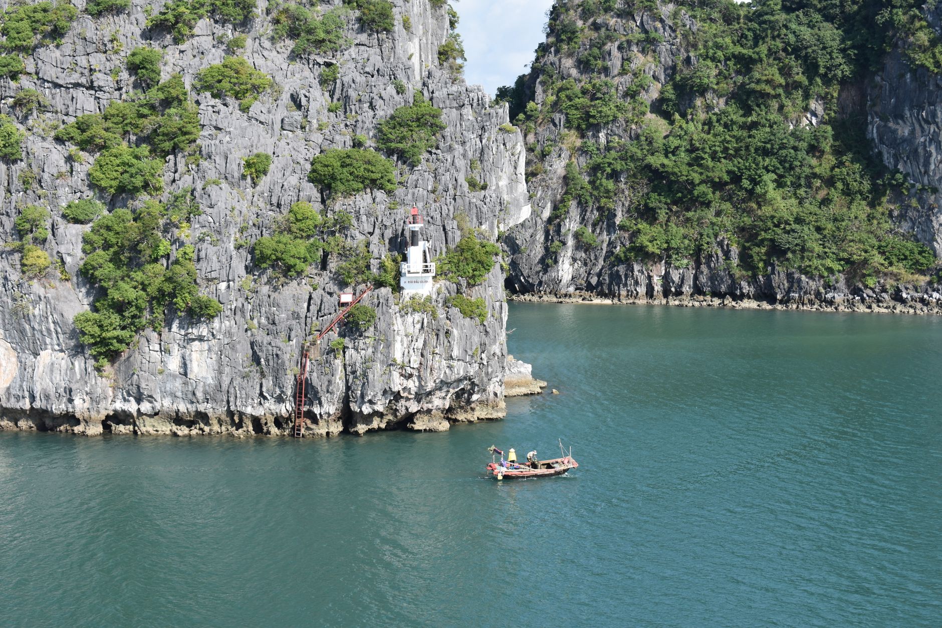 A breathtaking view of Halong Bay featuring a traditional fishing boat near rocky islets with lush greenery.