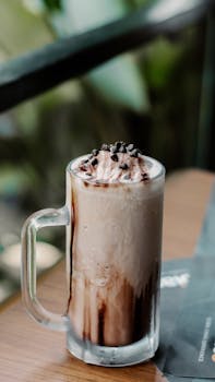 Delicious iced mocha in a glass mug topped with whipped cream and chocolate chips on a table.