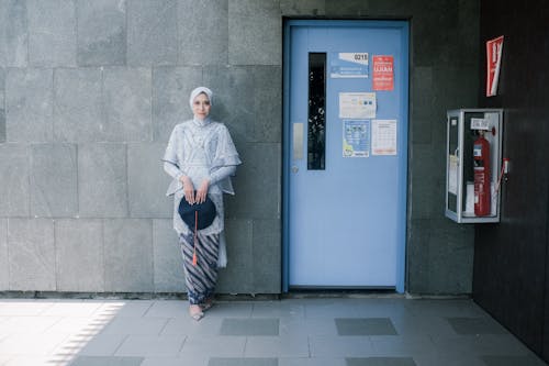 Woman in Hijab Holding Academic Hat and Standing by Wall