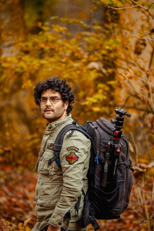 Free A man with a backpack and tripod stands amidst colorful autumn foliage, capturing nature. Stock Photo