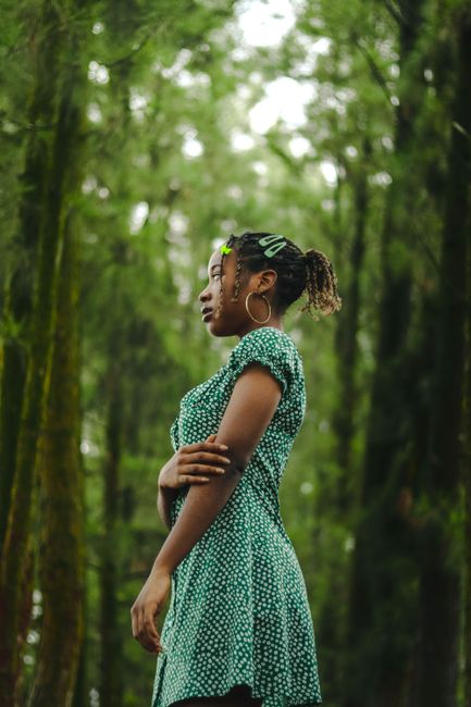 A graceful portrait of a woman in a green sundress standing in a lush forest setting.