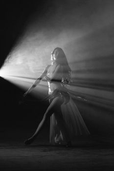 Graceful ballet dancer performing under dramatic lighting in a black and white setting.