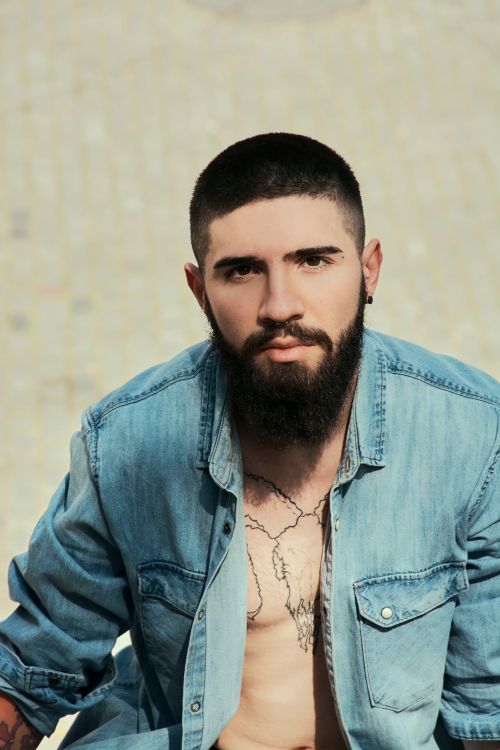 Free Bearded man in a denim shirt displays tattoos while posing outdoors. Stock Photo