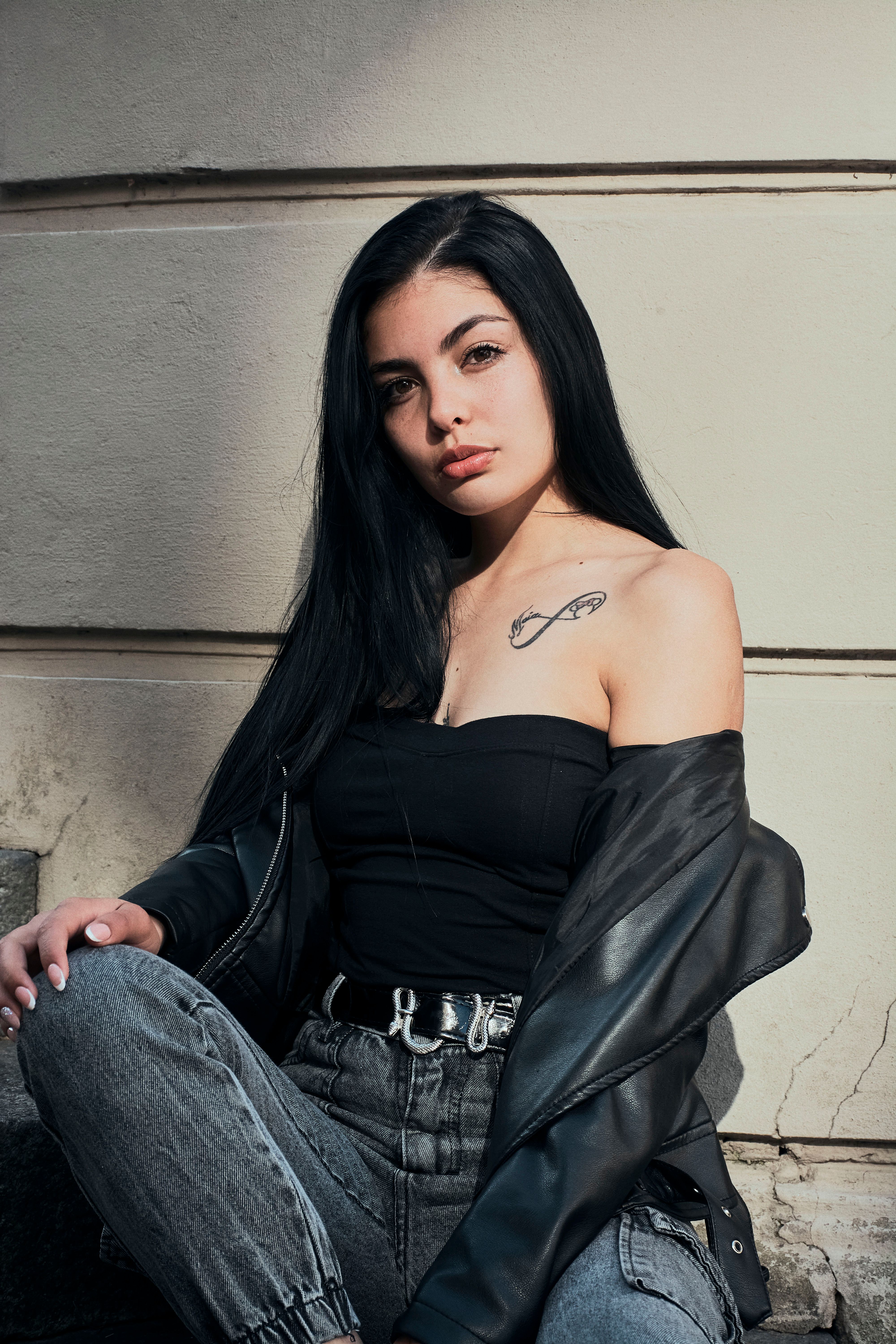 Stylish young woman in black outfit poses confidently, showcasing urban fashion and tattoos.