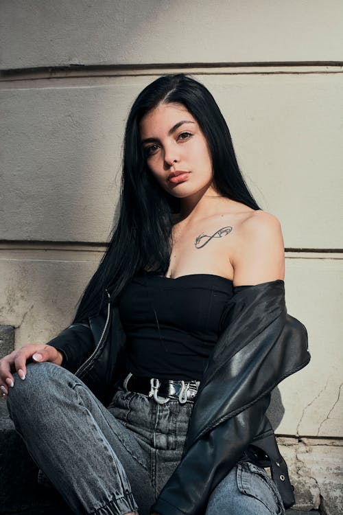 Model in a Leather Jacket Black Tube Top and Jeans Sitting Against a Wall