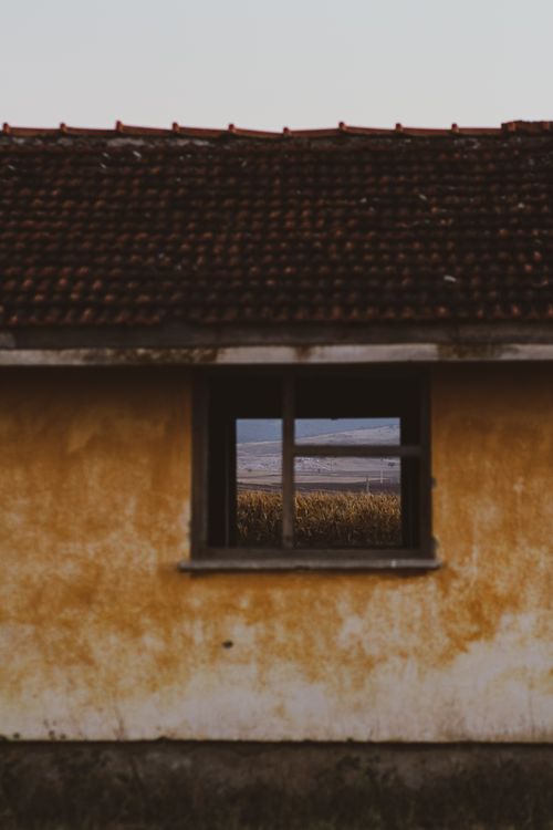 Free Rustic abandoned house with a window framing a scenic outdoor landscape, perfect for artistic photography. Stock Photo