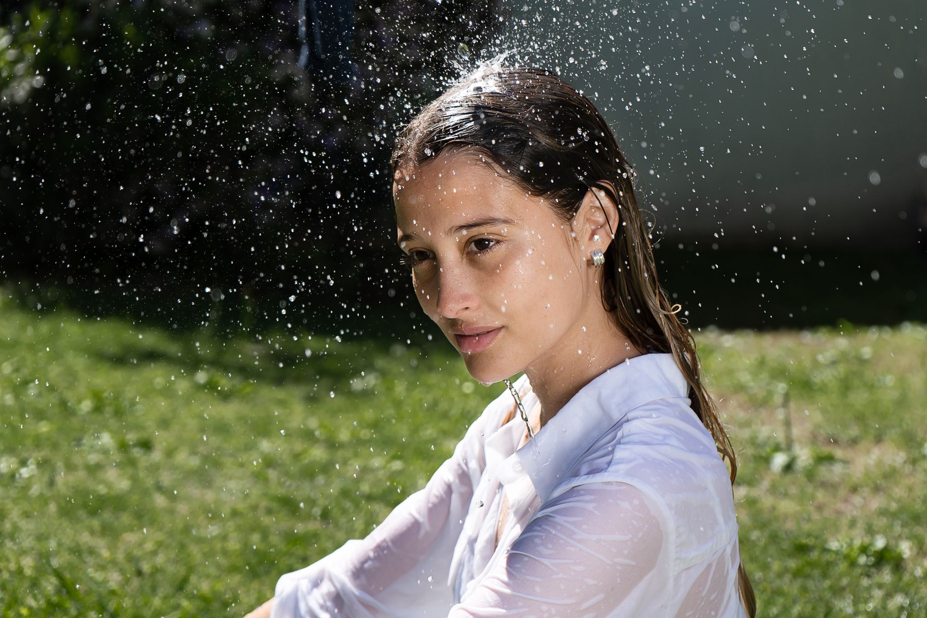 Portrait of a woman in a wet white shirt with water splashes outdoors in daylight.
