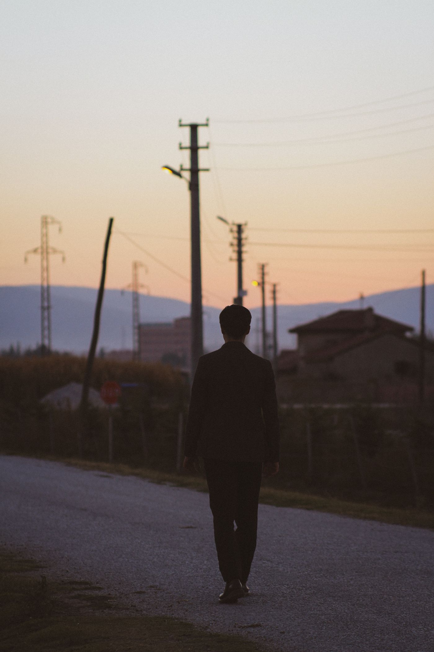 A lone figure walking along a road at dawn, silhouetted against the sky