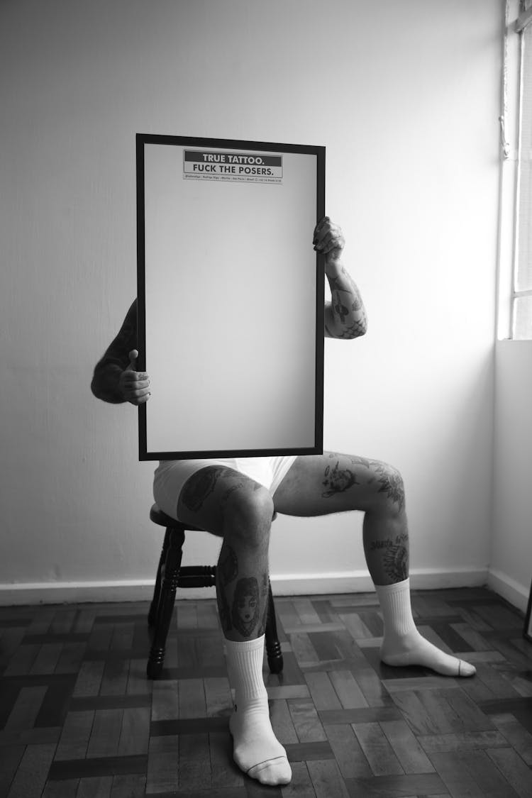 Man With Tattoos Sitting And Holding Frame