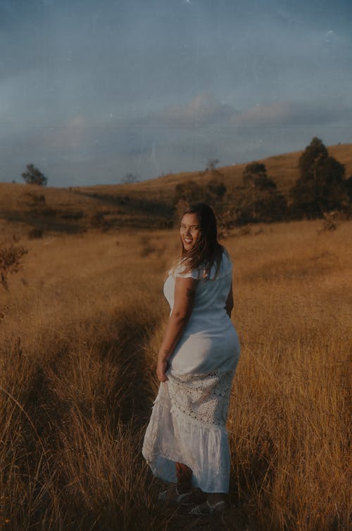 Young Woman in a White Dress Walking on a Meadow and Smiling 