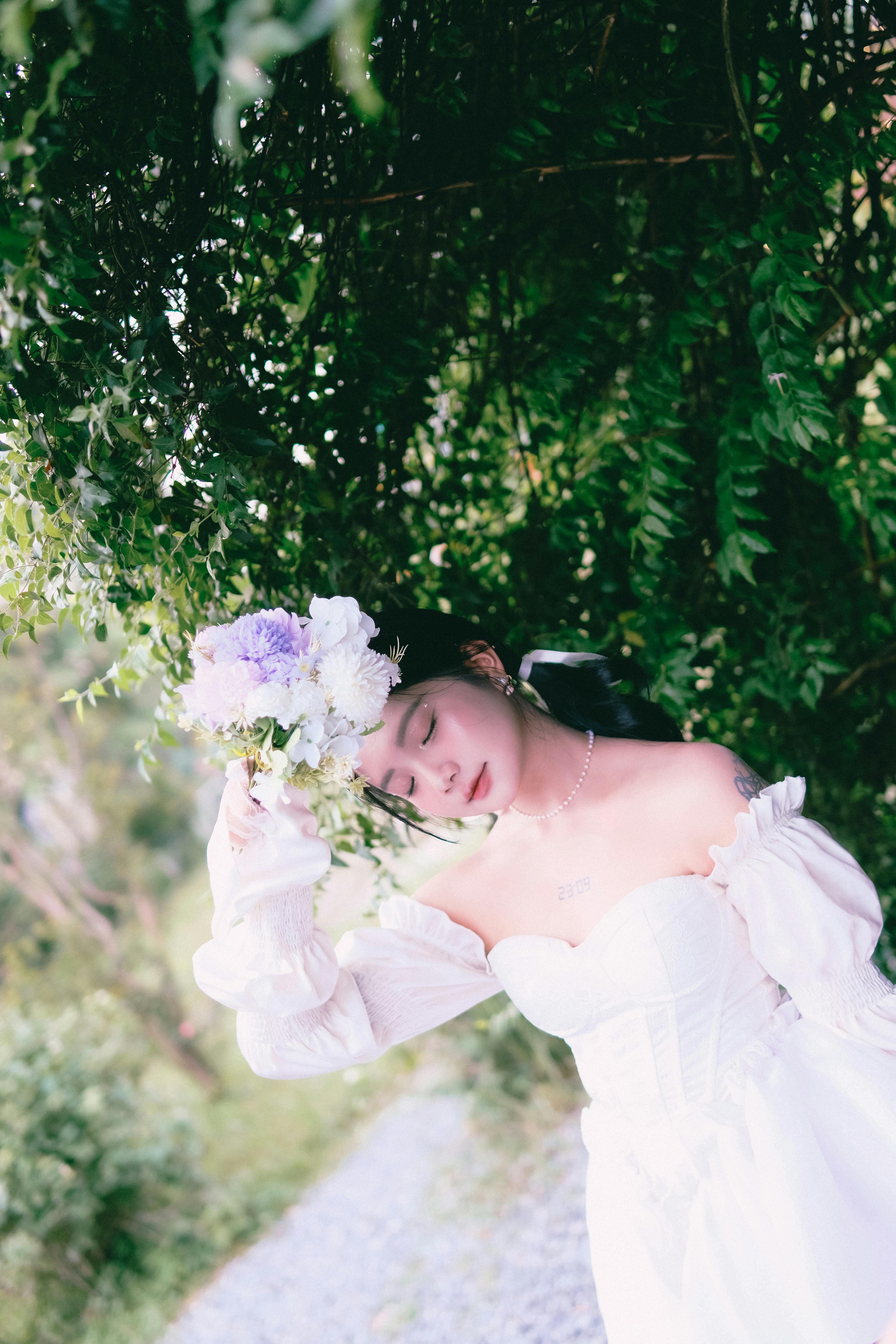 A serene bride in a wedding dress holds a bouquet in a lush garden setting, capturing an elegant moment.